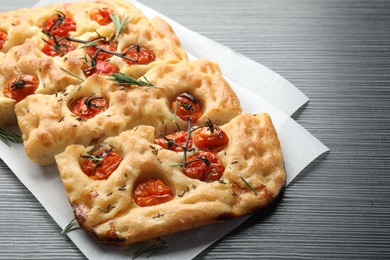Photo of Cut delicious focaccia with tomatoes and spices on dark wooden table, closeup