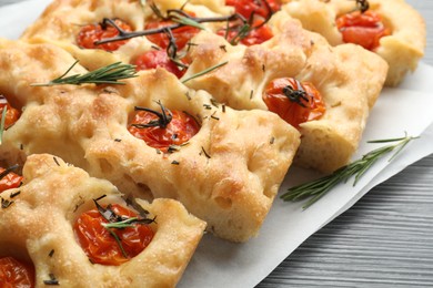 Photo of Cut delicious focaccia with tomatoes and spices on table, closeup