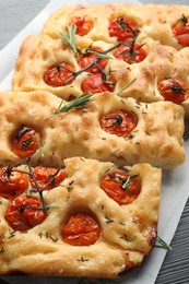 Photo of Cut delicious focaccia with tomatoes and spices on table, closeup