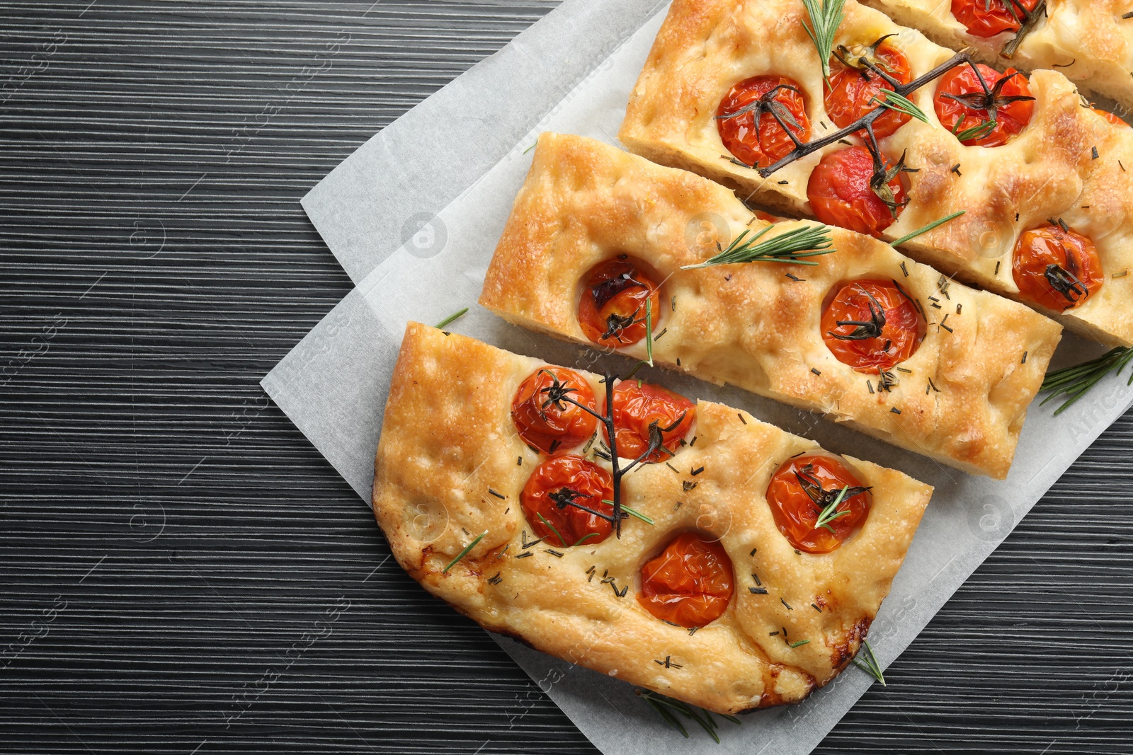 Cut delicious focaccia with tomatoes and spices on dark wooden table, top view Photo of Cut delicious focaccia with tomatoes and spices on dark wooden table, top view