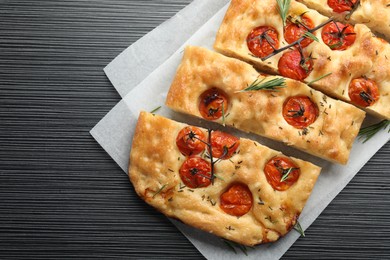 Photo of Cut delicious focaccia with tomatoes and spices on dark wooden table, top view
