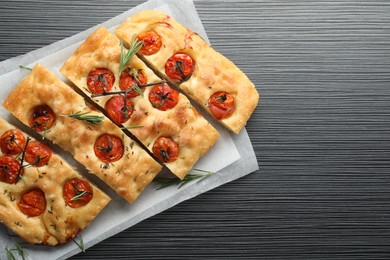 Photo of Cut delicious focaccia with tomatoes and spices on dark wooden table, top view. Space for text