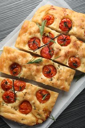 Photo of Cut delicious focaccia with tomatoes and spices on dark wooden table, top view