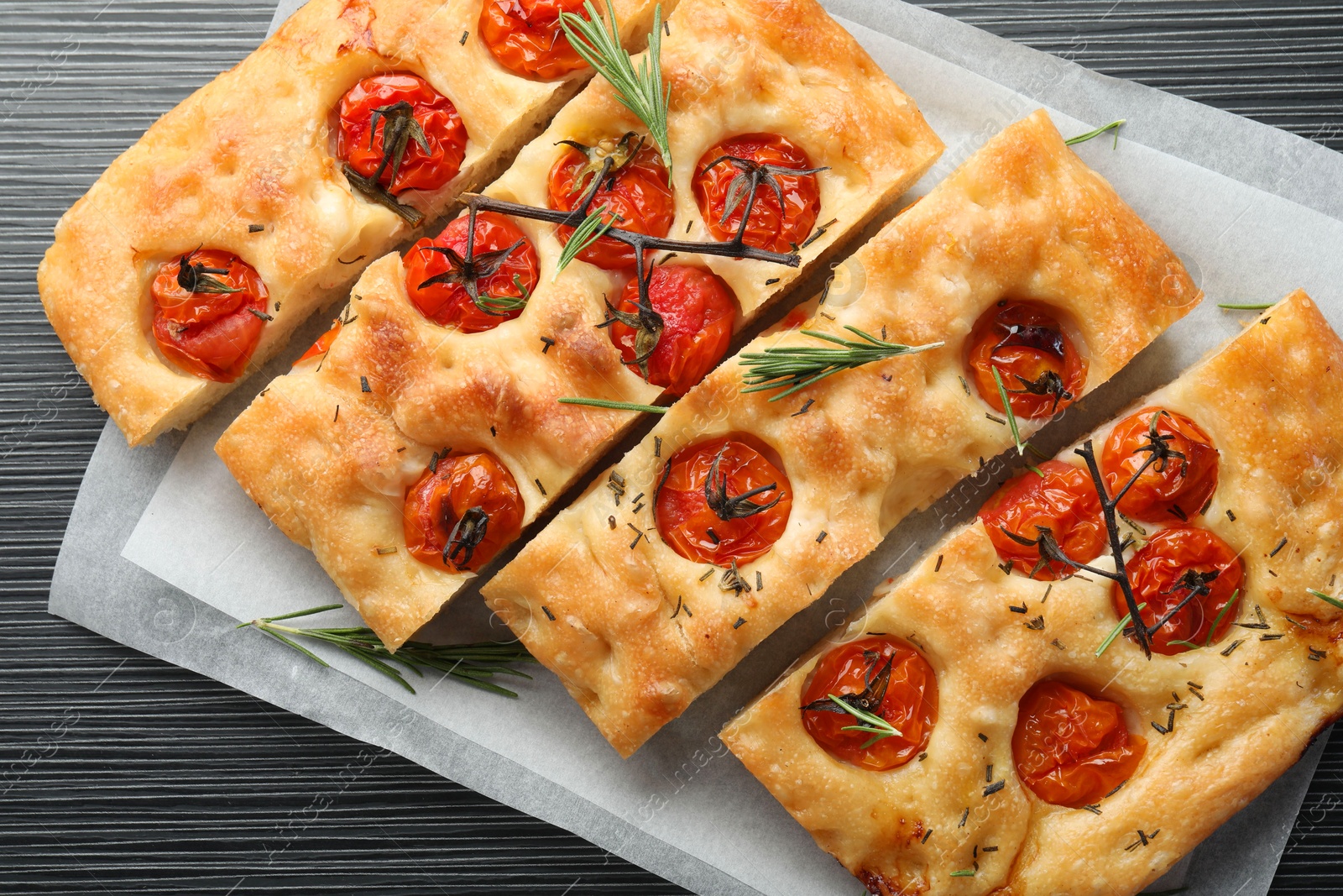 Cut delicious focaccia with tomatoes and spices on dark wooden table, top view Photo of Cut delicious focaccia with tomatoes and spices on dark wooden table, top view