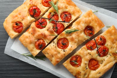 Photo of Cut delicious focaccia with tomatoes and spices on dark wooden table, top view