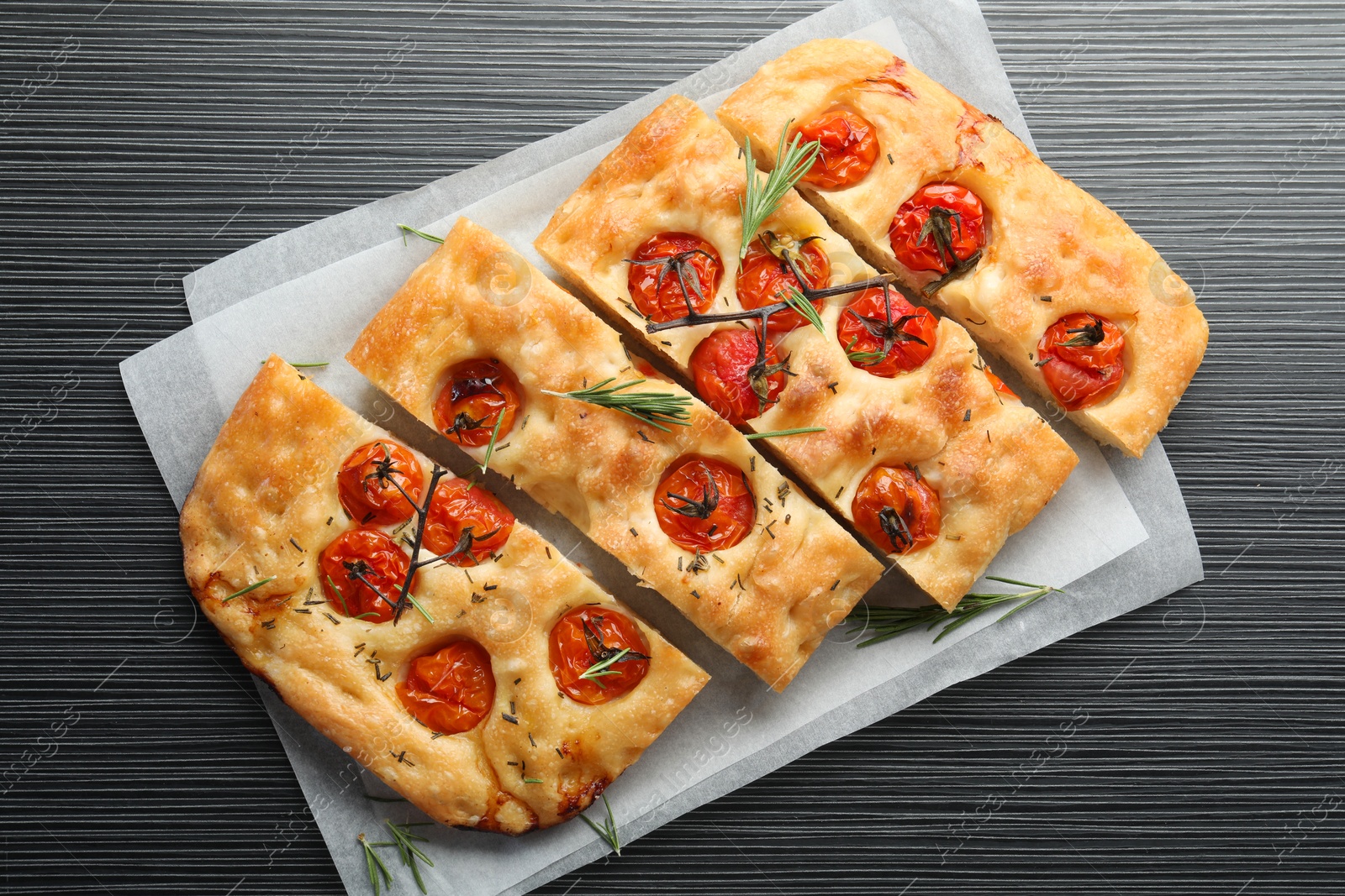 Cut delicious focaccia with tomatoes and spices on dark wooden table, top view Photo of Cut delicious focaccia with tomatoes and spices on dark wooden table, top view