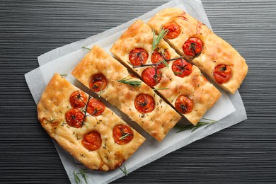 Photo of Cut delicious focaccia with tomatoes and spices on dark wooden table, top view