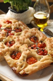 Photo of Cut delicious focaccia with tomatoes and spices on table, closeup
