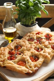 Photo of Cut delicious focaccia with tomatoes, spices and oil on table, closeup