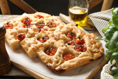 Photo of Cut delicious focaccia with tomatoes and spices on table, closeup