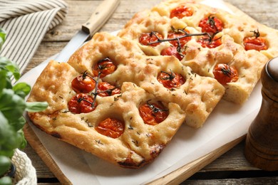 Photo of Cut delicious focaccia with tomatoes and spices on table, closeup