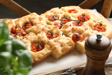 Photo of Cut delicious focaccia with tomatoes and spices on table, closeup
