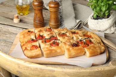 Photo of Cut delicious focaccia with tomatoes and spices on wooden table, closeup