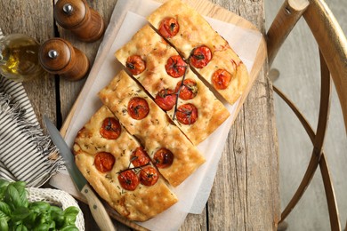 Photo of Cut delicious focaccia with tomatoes, spices and oil on wooden table, flat lay