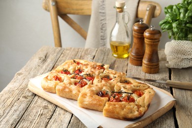Photo of Cut delicious focaccia with tomatoes, spices and oil on wooden table indoors