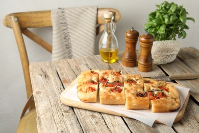 Photo of Cut delicious focaccia with tomatoes, spices and oil on wooden table indoors