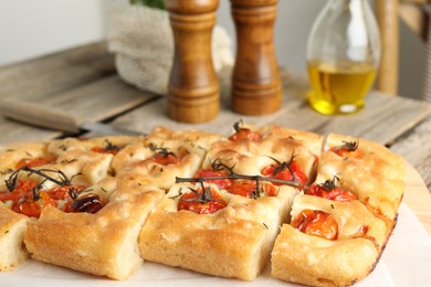 Photo of Cut delicious focaccia with tomatoes and spices on table, closeup