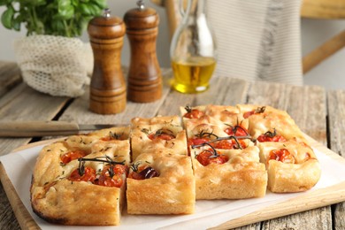 Photo of Cut delicious focaccia with tomatoes and spices on wooden table, closeup