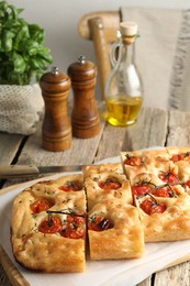 Photo of Cut delicious focaccia with tomatoes, spices and oil on wooden table indoors