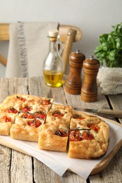 Photo of Cut delicious focaccia with tomatoes, spices and oil on wooden table indoors