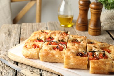 Photo of Cut delicious focaccia with tomatoes, spices and oil on wooden table indoors