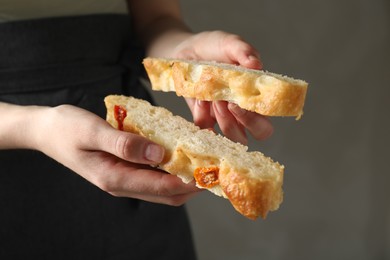 Photo of Woman holding pieces of delicious focaccia with tomatoes on gray background, closeup