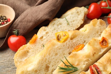 Photo of Cut delicious focaccia with tomatoes and rosemary on table, closeup