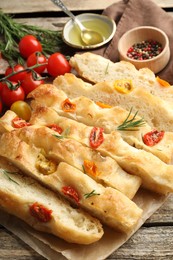 Photo of Cut delicious focaccia with tomatoes, spices and oil on wooden table, closeup