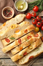 Photo of Cut delicious focaccia with tomatoes, spices and oil on wooden table, flat lay