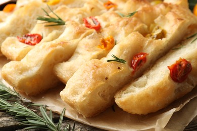 Photo of Cut delicious focaccia with tomatoes and rosemary on table, closeup