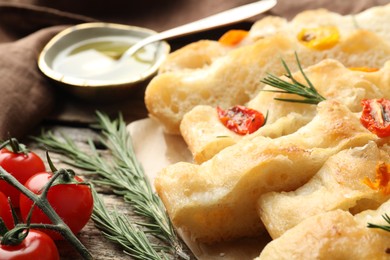 Photo of Cut delicious focaccia with tomatoes, rosemary and oil on table, closeup