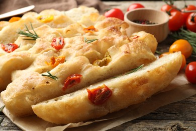 Photo of Cut delicious focaccia with tomatoes and rosemary on table, closeup