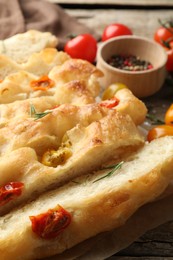Photo of Cut delicious focaccia with tomatoes and rosemary on table, closeup