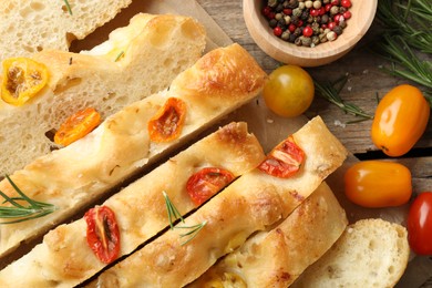 Photo of Cut delicious focaccia with tomatoes and spices on wooden table, flat lay
