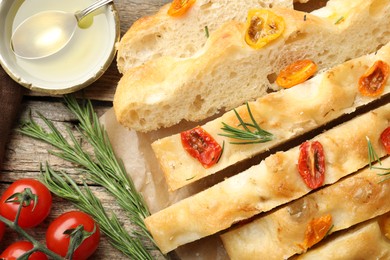Photo of Cut delicious focaccia with tomatoes, spices and oil on wooden table, flat lay