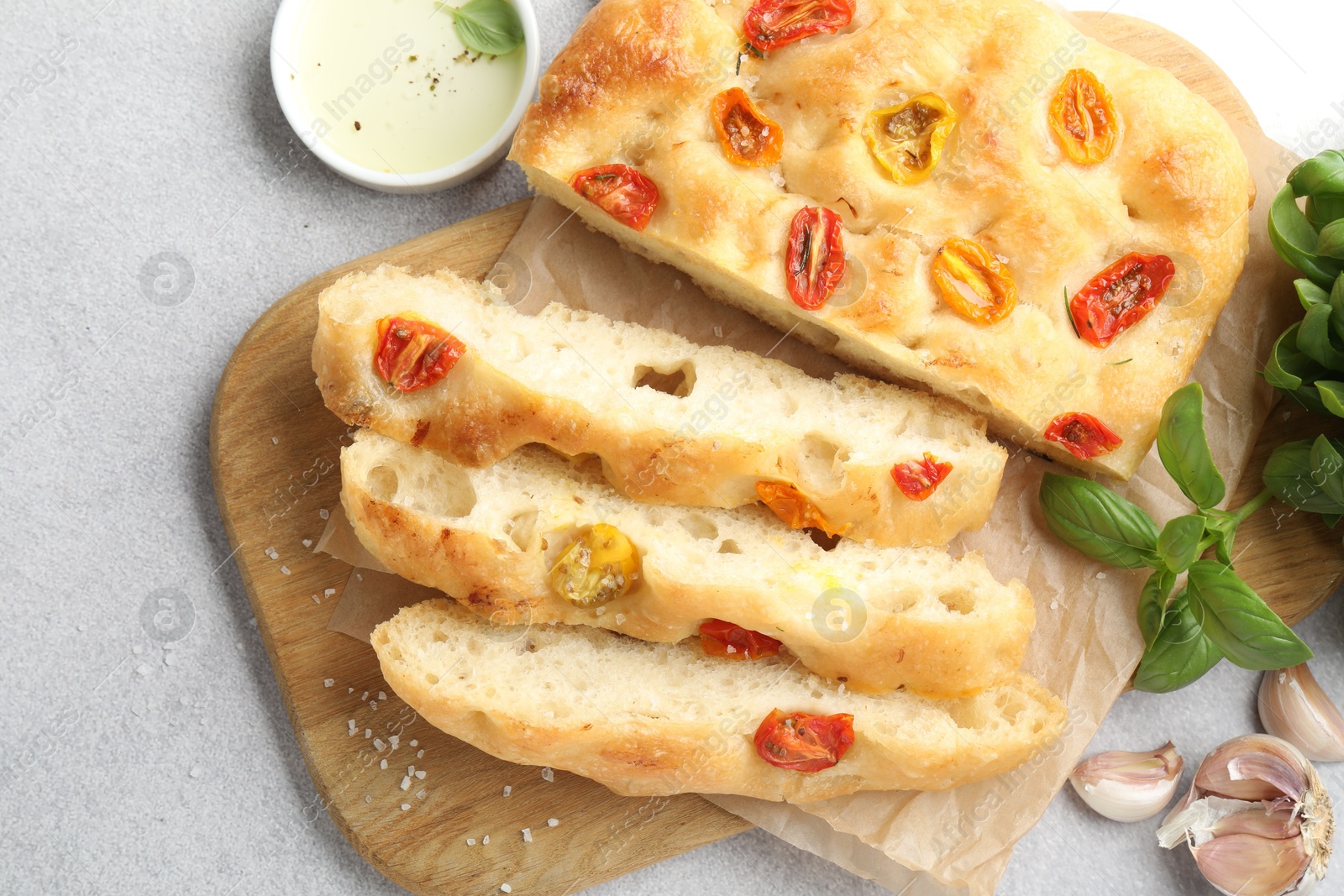 Cut delicious focaccia with tomatoes, spices and oil on gray table, flat lay Photo of Cut delicious focaccia with tomatoes, spices and oil on gray table, flat lay