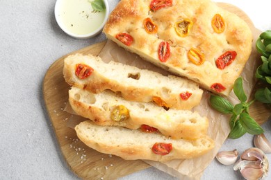 Photo of Cut delicious focaccia with tomatoes, spices and oil on gray table, flat lay