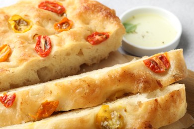 Photo of Cut delicious focaccia with tomatoes and oil on gray table, closeup