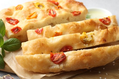Photo of Cut delicious focaccia with tomatoes and basil on table, closeup