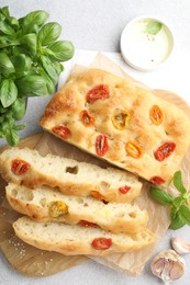 Photo of Cut delicious focaccia with tomatoes, spices and oil on gray table, flat lay