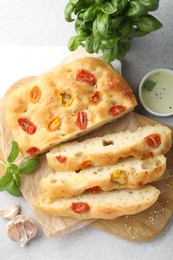 Photo of Cut delicious focaccia with tomatoes, spices and oil on gray table, flat lay