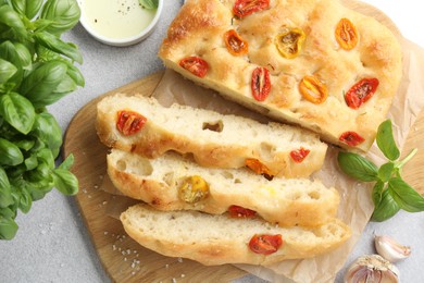Photo of Cut delicious focaccia with tomatoes, spices and oil on gray table, flat lay