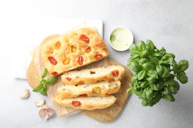 Photo of Cut delicious focaccia with tomatoes, spices and oil on gray table, flat lay