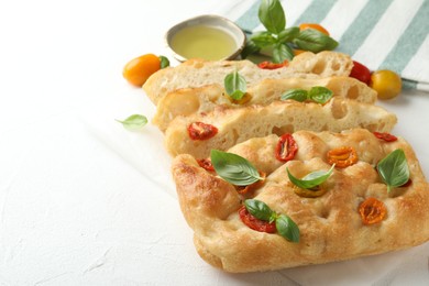 Photo of Cut delicious focaccia with tomatoes, basil and oil on light table, closeup. Space for text