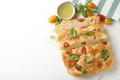 Photo of Cut delicious focaccia with tomatoes, basil and oil on light table, flat lay. Space for text