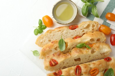 Photo of Cut delicious focaccia with tomatoes, basil and oil on light table, flat lay. Space for text