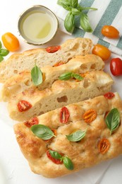 Photo of Cut delicious focaccia with tomatoes, basil and oil on table, flat lay