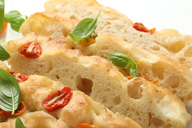 Photo of Cut delicious focaccia with tomatoes and basil on table, closeup