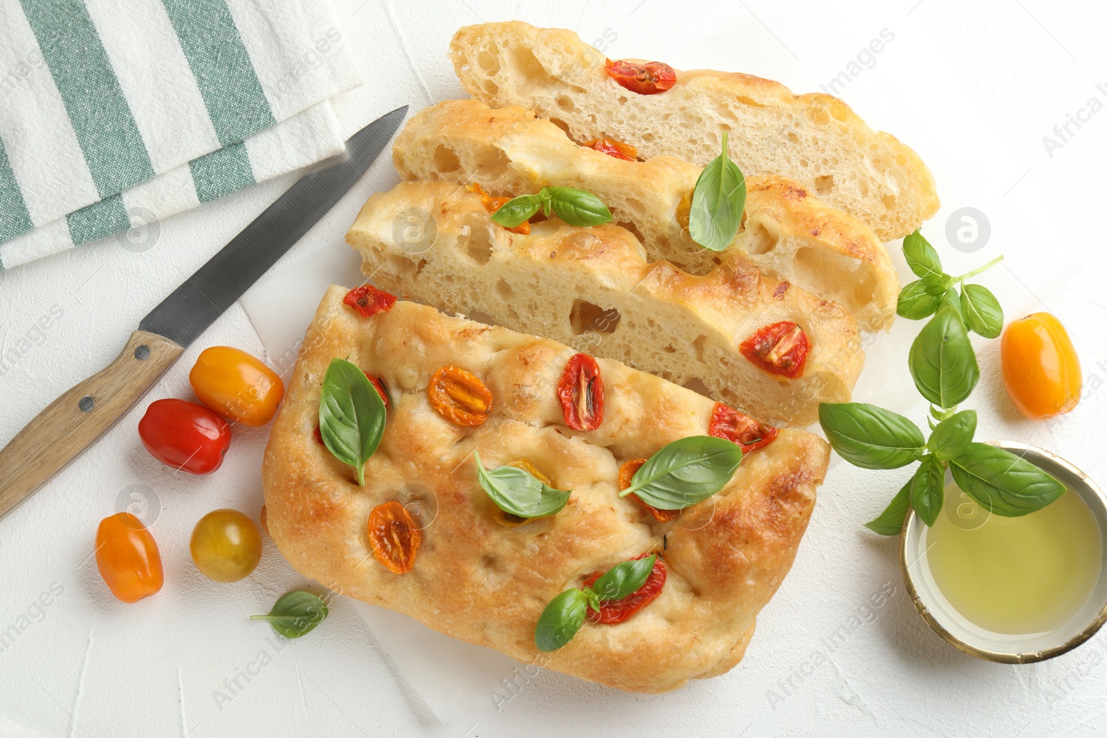 Cut delicious focaccia with tomatoes, basil, oil and knife on light table, flat lay Photo of Cut delicious focaccia with tomatoes, basil, oil and knife on light table, flat lay