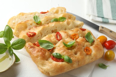 Photo of Cut delicious focaccia with tomatoes, basil, oil and knife on light table, closeup